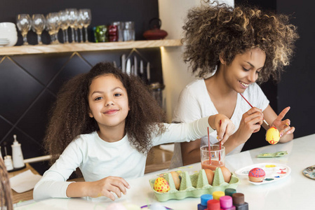 漂亮的非裔美国女人和她的女儿在厨房里给复活节彩蛋上色