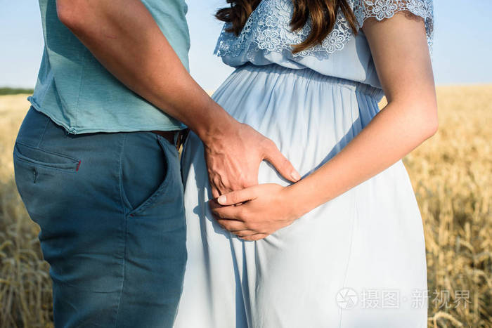 浪漫的怀孕夫妇拥抱在麦田里抱着一个肚子.