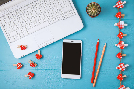 工作场所的蓝色笔记本电脑背景, 智能手机和红色装饰的心, 铅笔。情人节, 节日背景