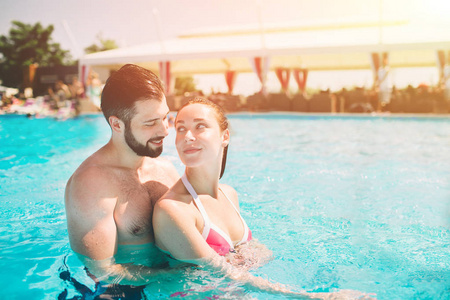 开朗年轻的男人和夫人休息, 而游泳池室外。夫妇在水中。男人做夏天 sephi