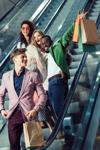 购物中心的自动扶梯上带包裹的年轻多民族购物者