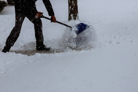在一个城市里,一个人在一场大雪后用铲子把雪从房子前面的人行道上铲