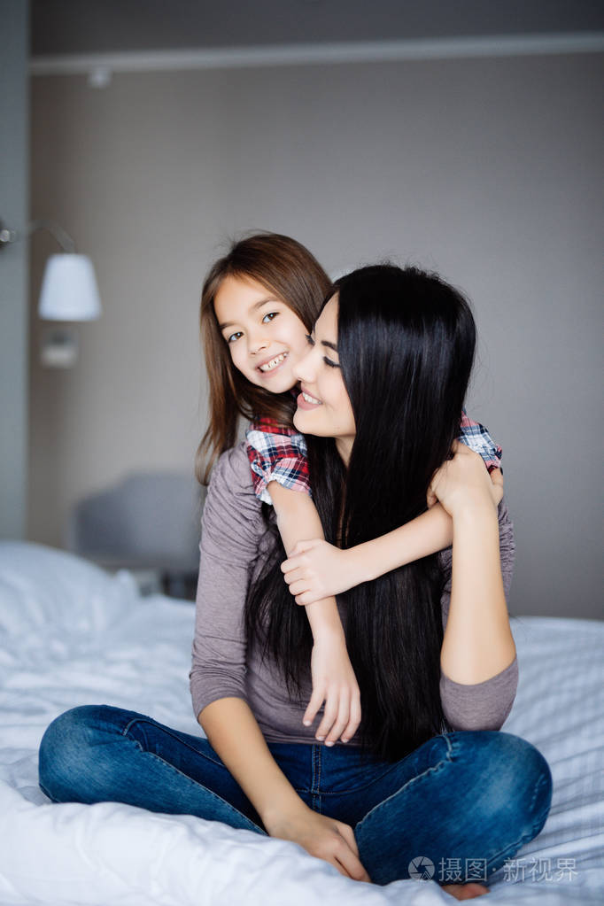 美丽的年轻女子和她迷人的小女儿在家里的床上拥抱和微笑