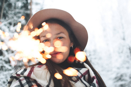 年轻美丽的女人在冬天的风景中享受她手中的孟加拉灯。 英俊的时髦女孩手里拿着火花。 戴着围巾和帽子