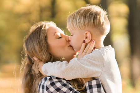 愉快的孩子男孩亲吻与妈妈在公园里在阳光下玩耍