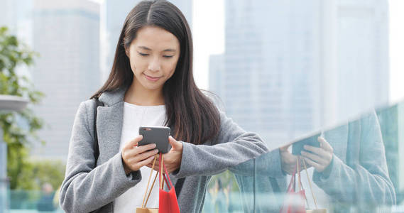 女人看手机，在户外拿着购物袋