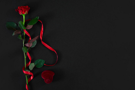 一朵暗红色的玫瑰, 红色的丝带和带戒指的盒子在黑色的 bac 上