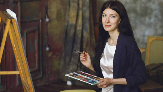 年轻的女艺术家绘制金龙与水彩颜料和刷子的画架画布
