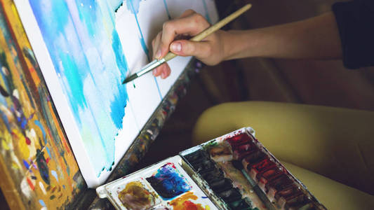 年轻的女艺术家绘制金龙与水彩颜料和刷子的画架画布特写手