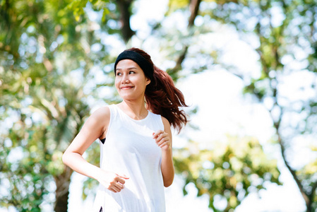 美丽快乐年轻健康的亚洲女人在早晨的阳光下在公园里奔跑照片