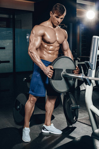 英俊的力量运动的人在节食训练抽肌肉用哑铃和杠铃。强壮的健美运动员, 完美的腹肌, 肩膀, 肱二头肌