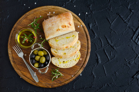 地中海小吃一套。 绿色和黑色橄榄橄榄油草药和切片的西巴塔面包在木板上的深色石头背景。 意大利食品概念。 上面的风景。 复制空间。