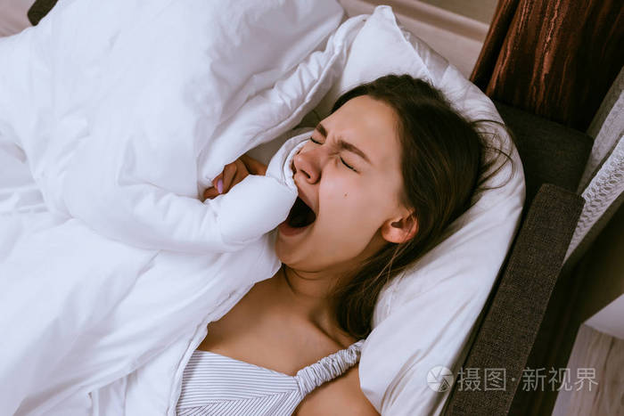 沉睡的年轻女孩躺在床上打呵欠清晨