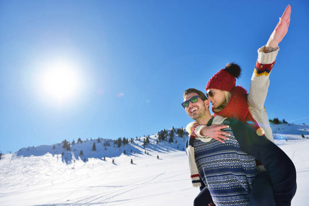 年轻夫妇在雪地上玩得很开心。快乐的男人在山上给他的微笑的女朋友背骑