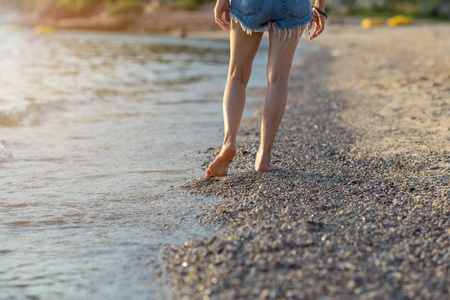 日落时在沙滩上行走的女人的腿
