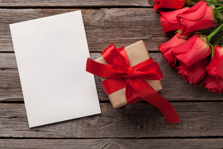 情人节贺卡上有红玫瑰和木桌上的礼品盒。带有文本的复制空间