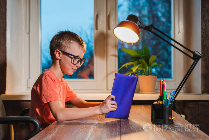 戴眼镜的孩子在带灯的桌子上看书.