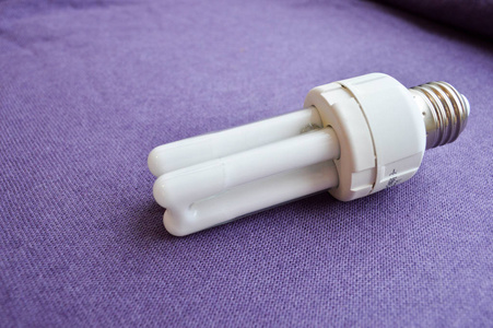 白色节能荧光灯灯泡，四管，银色盖在紫色布的背景上。
