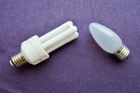两个灯泡。 白色节能荧光灯灯泡，四管，银基，长方形白炽灯泡，灰色玻璃在紫色布背景。