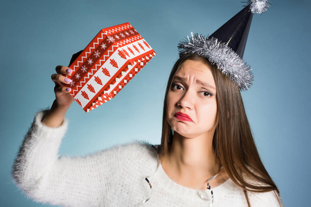 一个戴着节日帽子的沮丧女孩手里拿着一个空的礼品盒