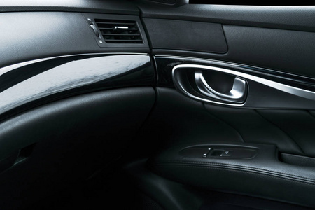汽车黑色穿孔皮革内部细节的门把手与窗户控制和调整。轿门把手里面的豪华现代轿车..开关按钮控制