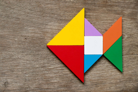 彩色七巧板拼图在木材背景下的鱼形照片