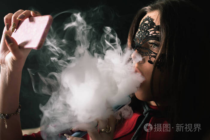 年轻, 漂亮的女孩与狂欢节面具抽烟的水烟