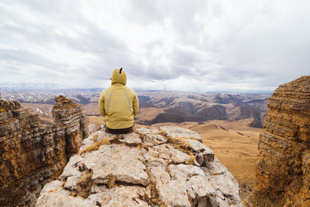 一个男性旅行者坐在悬崖边上, 享受高山自然, 放松和冥想
