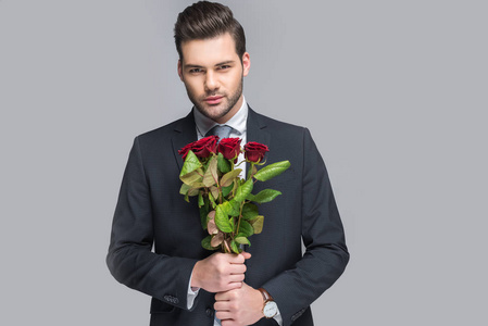 优雅的男人捧着一束红玫瑰，隔离在灰色上