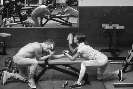 手臂摔跤夫妇，漂亮的微笑的女人，可爱的女孩，英俊的男人，男人，肌肉发达的躯干和的身体训练，在运动健身房，举重教练与水杯。