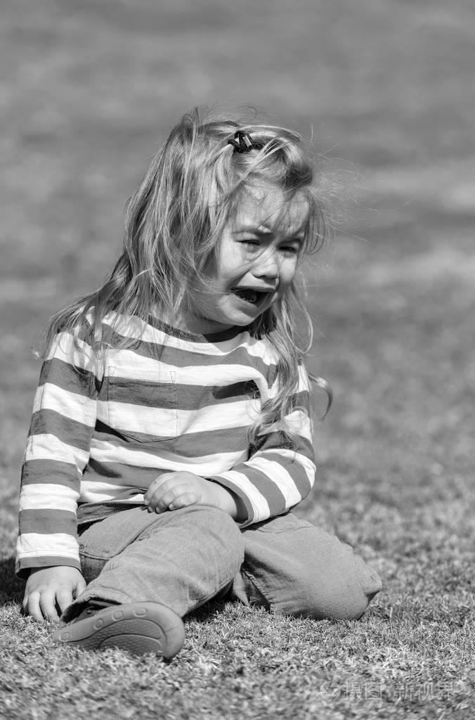 不开心的可爱的小宝贝男孩坐在公园里的绿草上