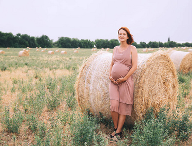 美丽的孕妇穿着自然。夏天，女人用干草堆在麦田的背景上举起双手。怀孕，生育，期望照片..妈妈在等孩子