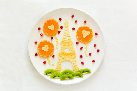 艺术食品概念。 埃菲尔铁塔，有一对情侣的剪影和心形球。 带石榴籽的花边煎饼。 上面的风景。 平躺着。 复制空间