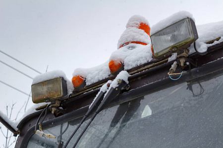老拖拉机二级前大灯与橙色警示灯特写镜头覆盖着雪