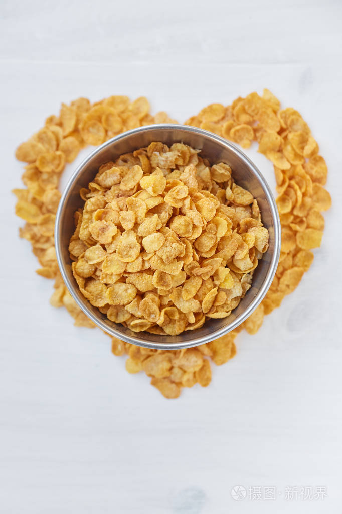 在一个彩色的白色木制背景的金属碗中的玉米片心的象征是用玉米片铺成