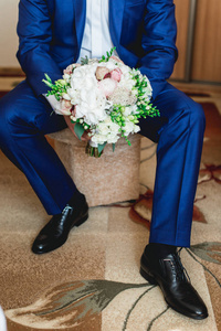 穿着深蓝色西装的未婚夫捧着一束牡丹花做成的结婚花束