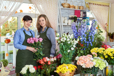 女性花卉销售商。两位迷人的年轻女性在花店里工作, 享受着美丽的花朵