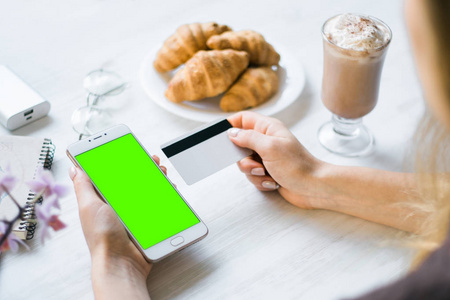 智能手机和信用卡借记卡在手的女孩智能手机绿色屏幕的色度键。互联网商务和网上购物的商品和服务支付