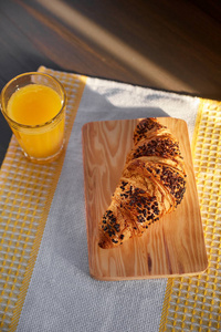 用一杯橙汁在木板和厨房巾上的新鲜羊角面包。在深色木桌上的刚出炉的羊角面包