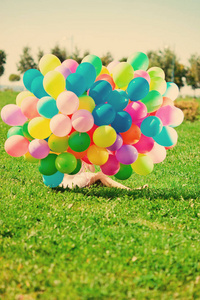 生日快乐的女人在天空中，手里拿着彩虹色的气球。阳光和积极的自然能量。公园草地上的年轻漂亮女孩。