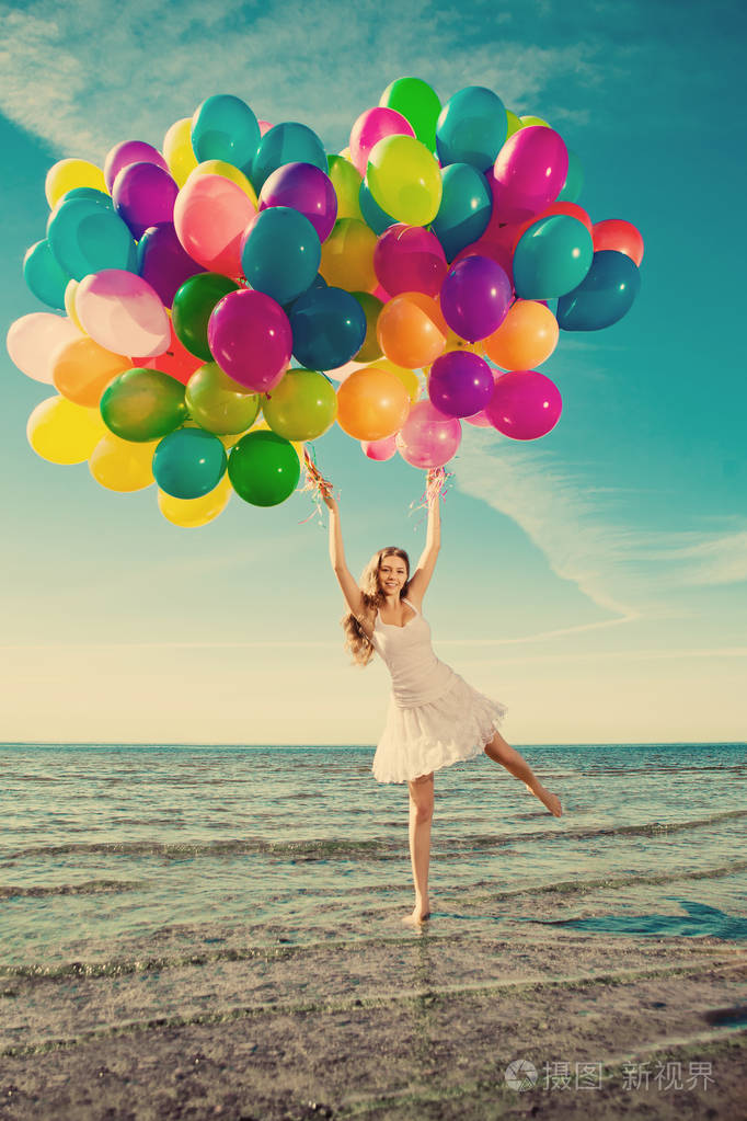 美丽的年轻时尚的女人,手里拿着多种颜色的彩虹气球对着天空.