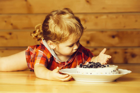 可爱的小男孩，金发碧眼的孩子，在木桌上吃着美味的蛋糕和蓝莓