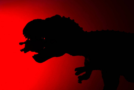 暴龙的影子在黑暗中咬着一只红色的小恐龙