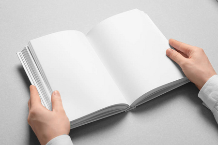 女人拿着一本空白页的书在浅色的背景上。 设计模拟