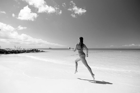 穿着泳衣在海水中奔跑的女人，阳光明媚的一天，在热带海滩运动和健康的概念