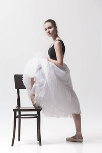 年轻的芭蕾舞女演员在白色的包姿势近椅子