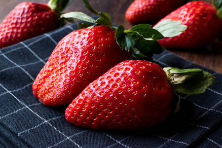 新鲜的有机成熟的两个草莓, 叶子在深色表面与桌布