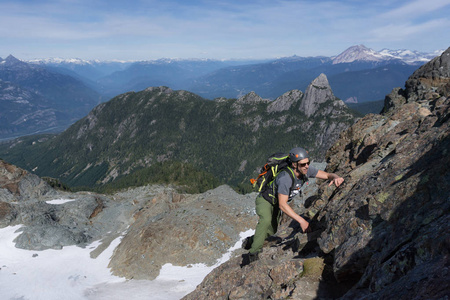 一个健康的年轻白种人冒险的人正在攀登一个陡峭的岩石板在一个美丽的夏天。 图片拍摄的上升到天空飞行员山附近的斯卡米什北部温哥华加拿