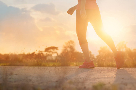 在夕阳背景下的乡村道路上的运动员女子步行运动