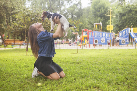 可爱的美丽的苗条白种人黑发女人，穿着休闲装裙子，衬衫和牛仔裤夹克在公园散步，在夏天和她可爱的杰克拉塞尔狗。他们充满了欢乐，微